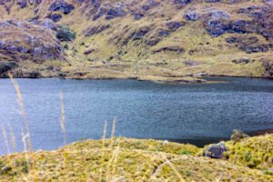Paisaje de montaña en el Parque Nacional Cajas, Azuay, con formaciones rocosas, neblina y una laguna al atardecer