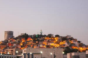 Vista nocturna del Cerro Santa Ana en Guayaquil con el faro iluminado, casas coloridas y edificios modernos en la base