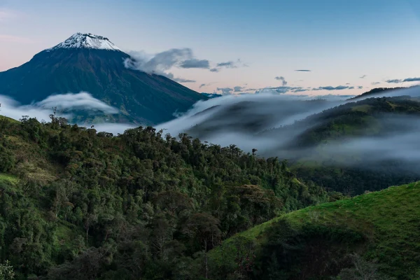 Vista del Volcán Tungurahua nevado con nubes bajas y bosque andino exuberante en la Avenida de los Volcanes, Ecuador