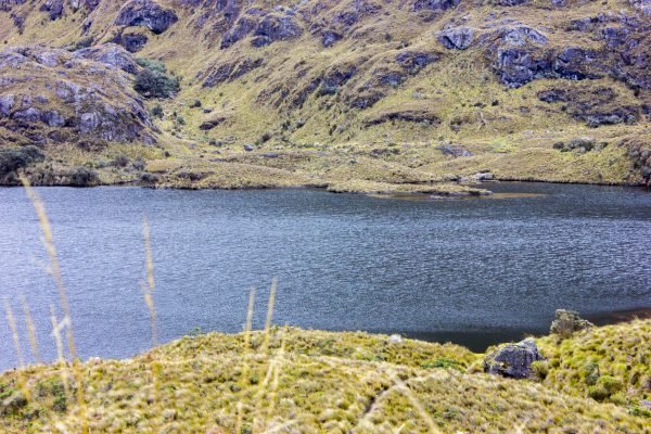 Paisaje de montaña en el Parque Nacional Cajas, Azuay, con formaciones rocosas, neblina y una laguna al atardecer